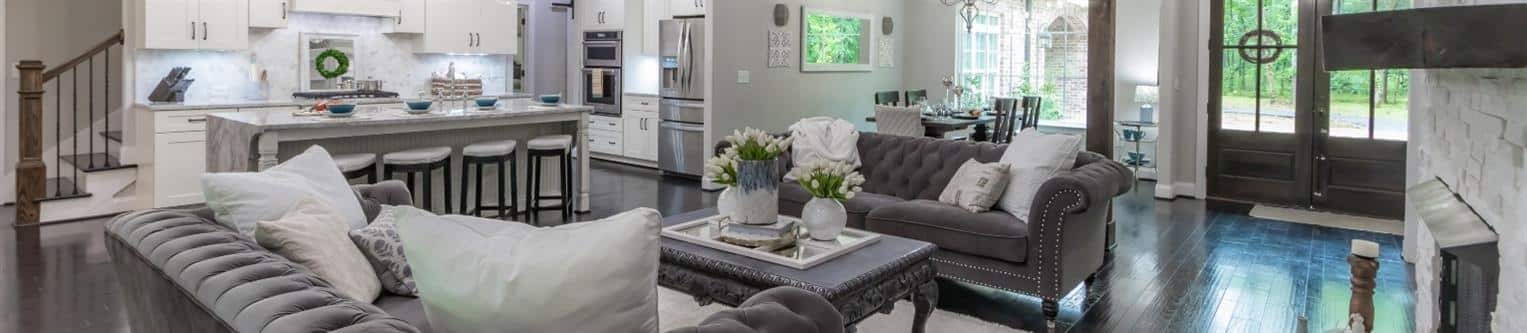 Wide photo of new construction living area with grey couches and dark wood floor