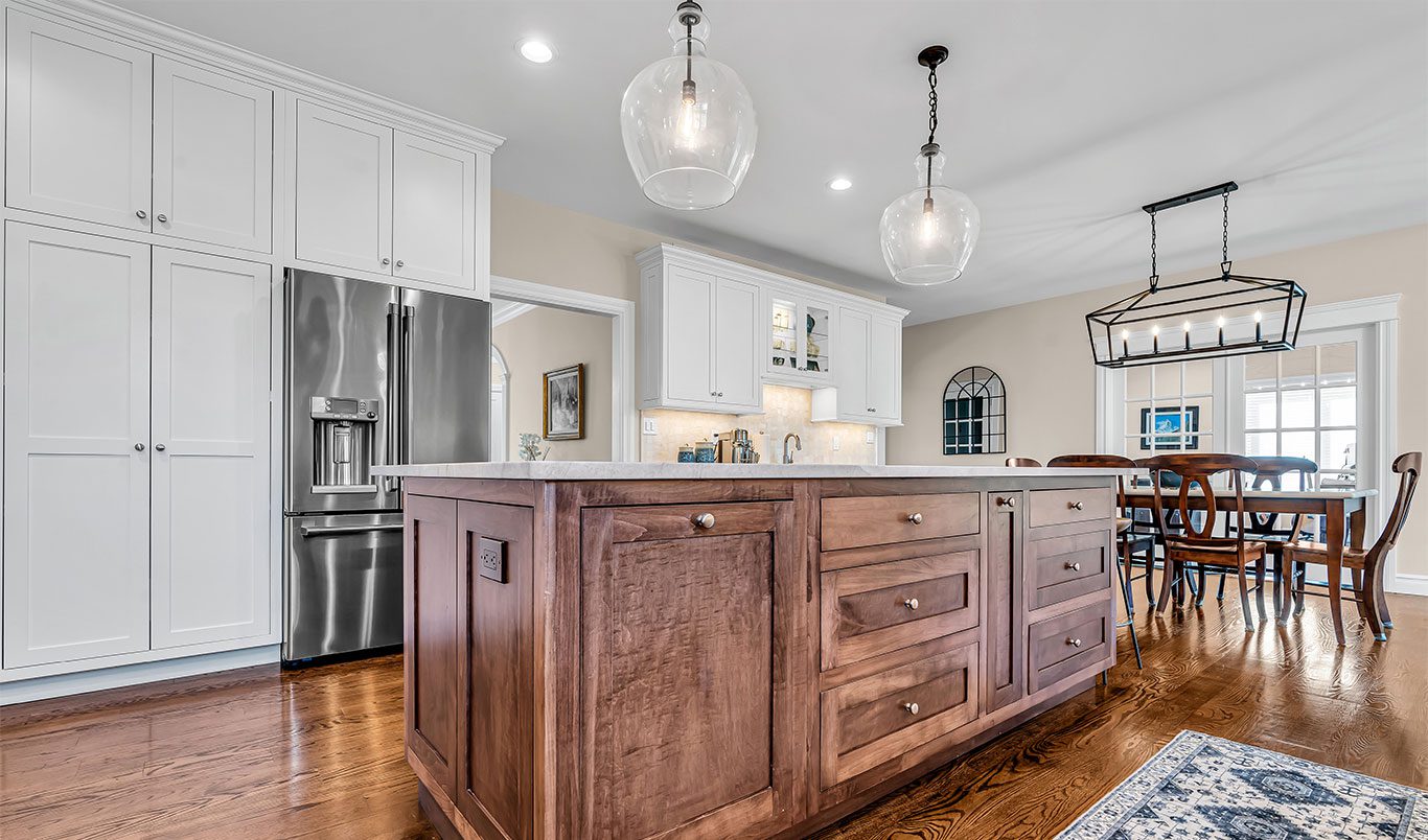 Modern white kitchen with large dark wood island and dining table in the background