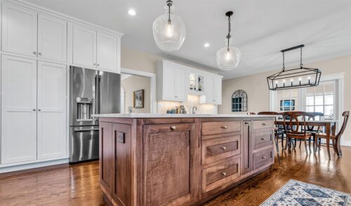 Modern white kitchen with large dark wood island and dining table in the background